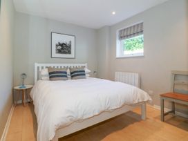 A bedroom with a white bed and striped pillows a bedside table with a lamp a window and a chair at St Tudwals View in Abersoch