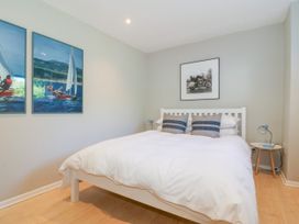 A bedroom with a white bed and pillows two paintings on the wall and a small round side table with a lamp at St Tudwals View in Abersoch