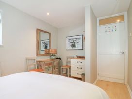 A bedroom corner with a bed, two chairs, a rustic cabinet with a lamp, a chest of drawers, a wall mirror, and a door at St Tudwals View in Abersoch