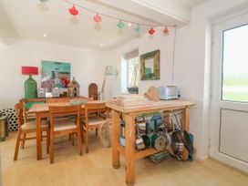A dining area with wooden table and chairs a side table with pots pans and a toaster and a sideboard with a lamp and artwork at St Tudwals View in Abersoch