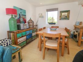 A dining room with a wooden table and chairs a sideboard with colorful drawers and a decorative boat on the window sill at St Tudwals View in Abersoch