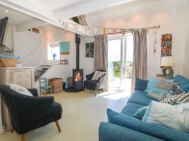 A living room with a blue sofa and black armchairs near a wood burning stove and sliding glass doors at St Tudwals View in Abersoch