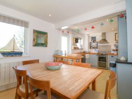 A kitchen and dining area with wooden table and chairs having a decorative bowl on the table and a model sailboat on the window sill at St Tudwals View in Abersoch