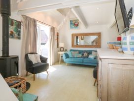A living room with a blue sofa black armchair wood stove and a wall mounted television at St Tudwals View in Abersoch