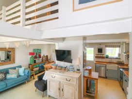 An open-plan living area with a blue sofa and black armchair a wall-mounted TV a kitchen with wooden countertops and appliances at St Tudwals View in Abersoch
