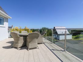 An outdoor balcony with wicker chairs and glass railing overlooking a residential area at St Tudwals View in Abersoch