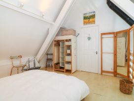 A bedroom with a white bed a small open wardrobe a full length mirror and two chairs at St Tudwals View in Abersoch