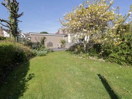 A garden with green grass, flowering trees and shrubs, a wooden fence and a concrete shed with garden furniture at Hafan Y Mor in Rhos-on-Sea