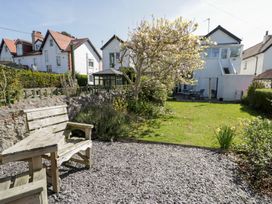 A garden with wooden benches gravel area flowers and a tree with houses in the background at Hafan Y Mor in Rhos-on-Sea