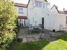 A patio area with outdoor table and chairs and potted plants next to a white house with garden at Hafan Y Mor in Rhos-on-Sea