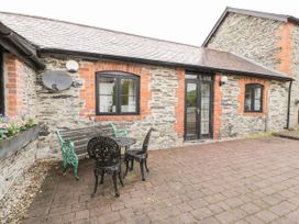 A stone building with black framed windows and a door with outdoor metal chairs and a bench on a paved patio at The Dairy in Carrog near Corwen