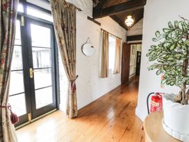 A hallway with wooden floor two windows with curtains a round mirror a door and a plant in a white pot at The Dairy in Carrog near Corwen