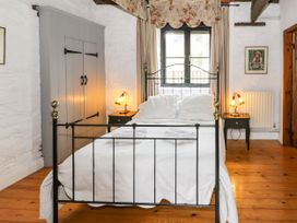 A bedroom with a black metal bed frame white bedding two bedside tables with lamps a grey wardrobe and a window with floral curtains at The Dairy in Carrog near Corwen