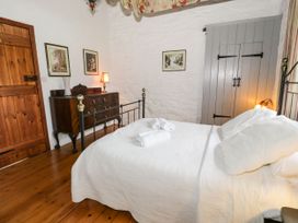 A bedroom with a wooden floor a bed with white bedding a wooden door a wooden dresser and framed pictures on the walls at The Dairy in Carrog near Corwen