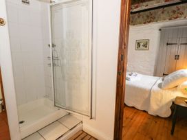 A tiled shower with a glass door next to a bedroom with a bed and wardrobe at The Dairy in Carrog near Corwen