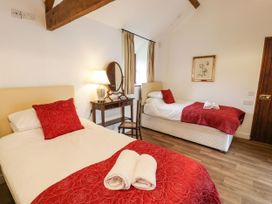 A bedroom with two single beds red pillows and bed covers a wooden desk with a lamp an oval mirror and a chair at The Dairy in Carrog near Corwen