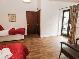 A bedroom with two single beds with red covers a wooden door a window with floral curtains and a chair at The Dairy in Carrog near Corwen