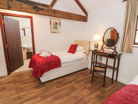 A bedroom with two single beds in white and red bedding a wooden dressing table with a mirror and lamp and a wooden floor at The Dairy Carrog near Corwen