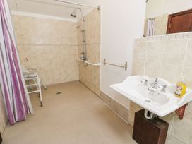 A bathroom with a walk in shower chair shower curtain and a washbasin with soap at The Dairy in Carrog near Corwen