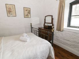 A bedroom with a bed covered by a white quilt and folded towels on top a wooden dresser with a mirror curtains and a window on white textured walls at The Dairy in Carrog near Corwen