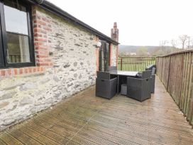 An outdoor wooden deck with black wicker furniture next to a stone wall and railing at The Dairy in Carrog near Corwen