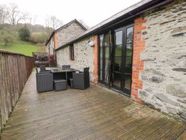An outdoor wooden deck with a table and six chairs next to a stone building at The Dairy in Carrog near Corwen