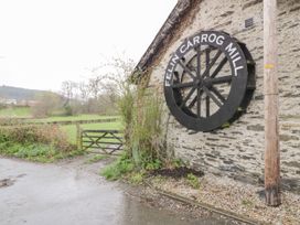 An exterior stone wall with a large black wheel sign reading felin carrog mill next to a wooden gate and green fields at The Dairy in Carrog near Corwen