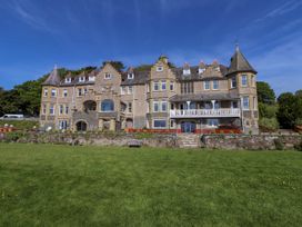A large stone building with multiple windows and pitched roofs with turrets with a grassy lawn in front at Menai View near Menai Bridge