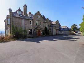 A stone building with multiple windows and chimneys with a paved driveway and parked cars near Menai Bridge
