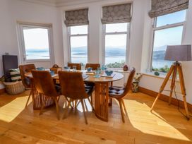 A dining area with a wooden table and six brown chairs next to windows showing a water view at Menai View near Menai Bridge