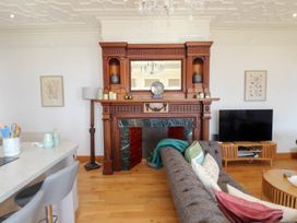 A living room with a wooden fireplace a grey sofa a television on a wooden stand and bar stools at Menai View near Menai Bridge