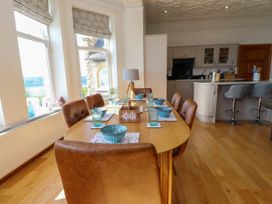 A dining area with a wooden table set with blue bowls and glasses and brown chairs next to large windows and an open kitchen at Menai View near Menai Bridge