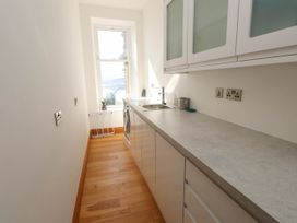 A narrow kitchen with wooden floor and white cabinets near a window at Menai View near Menai Bridge