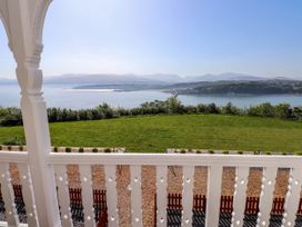 A view of a grassy lawn and body of water with hills in the background from a balcony with white railing at Menai View near Menai Bridge
