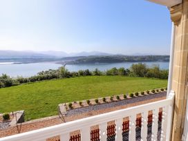 A view of a grassy lawn overlooking a body of water with hills and a bridge in the distance taken from a balcony at Menai View near Menai Bridge