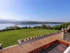A grassy garden with shrubs overlooking a body of water with hills and a bridge near Menai Bridge