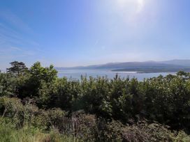 A view of a body of water with hills in the background and bushes in the foreground at Menai View near Menai Bridge