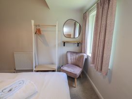A bedroom with a bed, chair, clothing rack, and mirror at Yew - Woodland Cottages, Bowness-On-Windermere