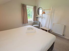 A bedroom with a bed, window, chair, and coat rack at Yew - Woodland Cottages, Bowness-On-Windermere