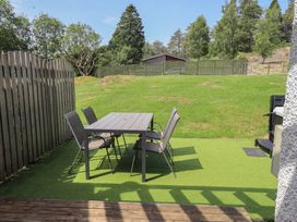 A table and chairs on grass with a shed in the background at Yew - Woodland Cottages Bowness-On-Windermere