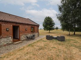 A patio area with chairs and a table beside a brick house at The Annexe in Litcham