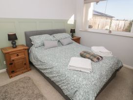 A bedroom with a double bed and green patterned bedding two wooden bedside tables with lamps and a window at Chy Bean in Abergele