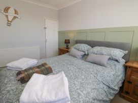 A bedroom with a bed with patterned bedding two wooden nightstands with a lamp and folded towels on the bed at Chy Bean in Abergele