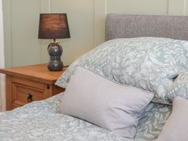 A bed with floral patterned bedding and pillows next to a wooden nightstand with a dark lamp at Chy Bean in Abergele