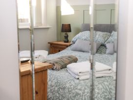 A bedroom with a bed covered in floral bedding towels and a blanket on the bed a wooden bedside table with a lamp by the window at Chy Bean in Abergele