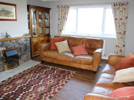 A living room with leather sofas a patterned rug a wooden cabinet and a stone fireplace at Pen Y Cae in Llansannan