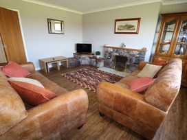 A living room with leather sofas a patterned rug a stone fireplace and a wooden cabinet at Pen Y Cae in Llansannan