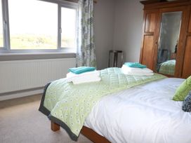 A bedroom with a bed with green patterned bedding and towels stacked on top next to a wooden wardrobe with a mirror at Pen Y Cae in Llansannan