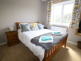 A bedroom with a wooden double bed with white bedding and pillows next to a window with patterned curtains at Pen Y Cae in Llansannan