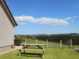 A wooden picnic table on grass next to a house with a view of green fields and hills at Pen Y Cae in Llansannan